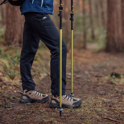 Person hiking in a forest with yellow hiking poles and dark pants with brown hiking boots.