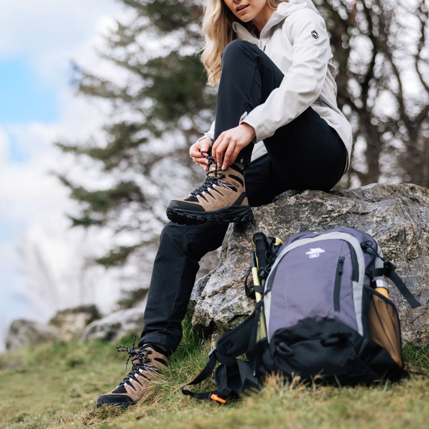 Person sitting on a rock with hiking boots and backpack, preparing for a hike.