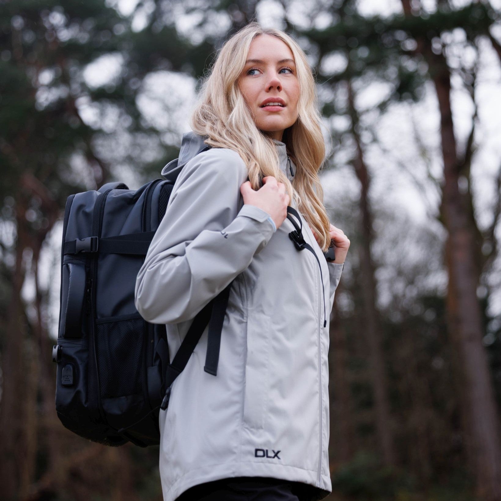 Woman in a gray jacket with a black backpack in a forest setting